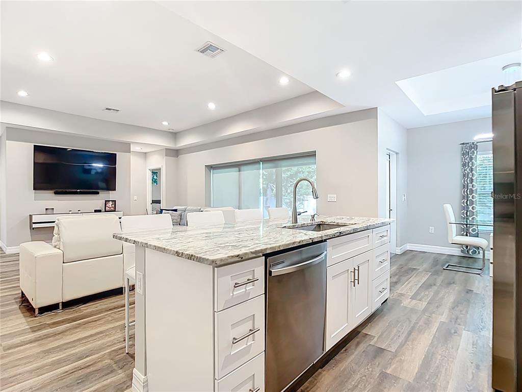 A kitchen island with a granite countertop and stainless steel dishwasher faces a living room — 5153 PINSON DRIVE, NORTH PORT, FL