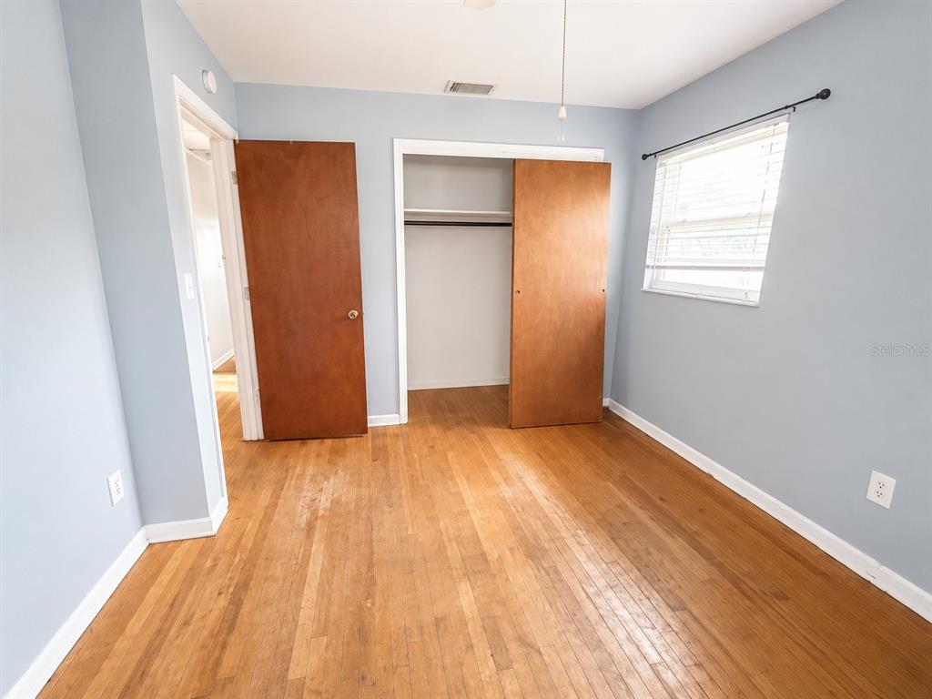 A bedroom features light blue walls, hardwood floors, a closet, and a window with blinds — 409 MONTGOMERY AVENUE, LAKELAND, FL
