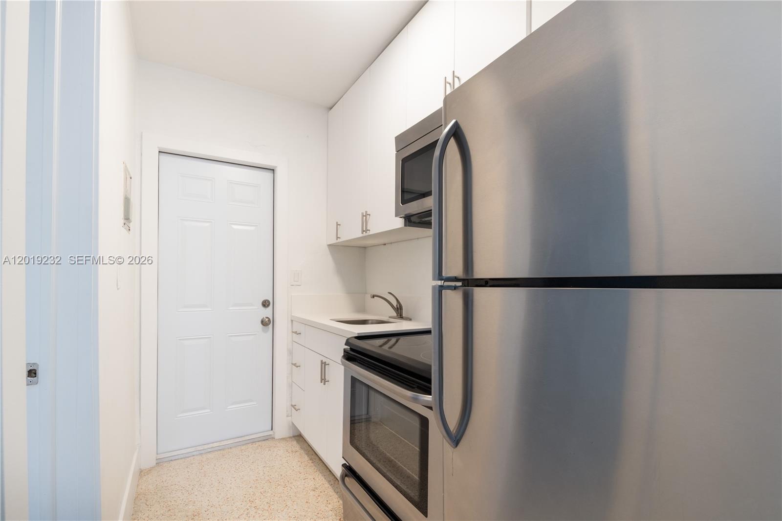 A small kitchen features white cabinets, stainless steel appliances, and a white door — 1450 SW 6th St # 9, Miami FL 33135, MIAMI, FL
