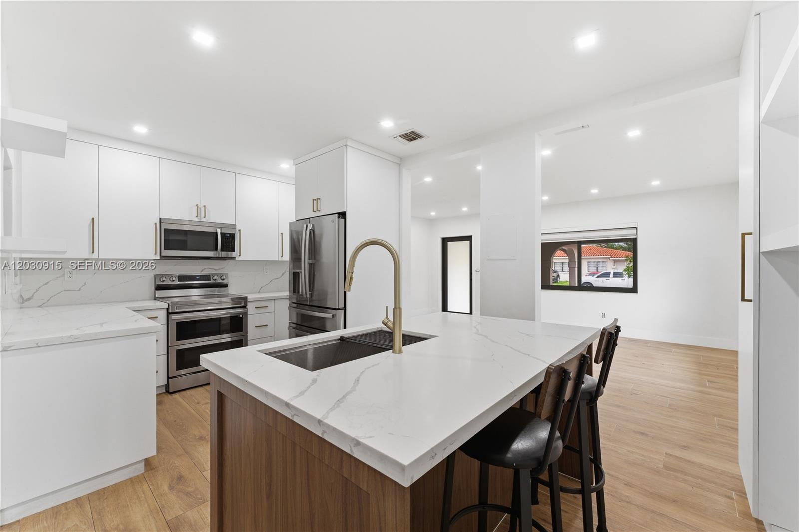 A modern kitchen features white cabinetry, a marble-topped island with seating, and wood-look flooring — 121 SW 71st Ave, Miami FL 33144, MIAMI, FL