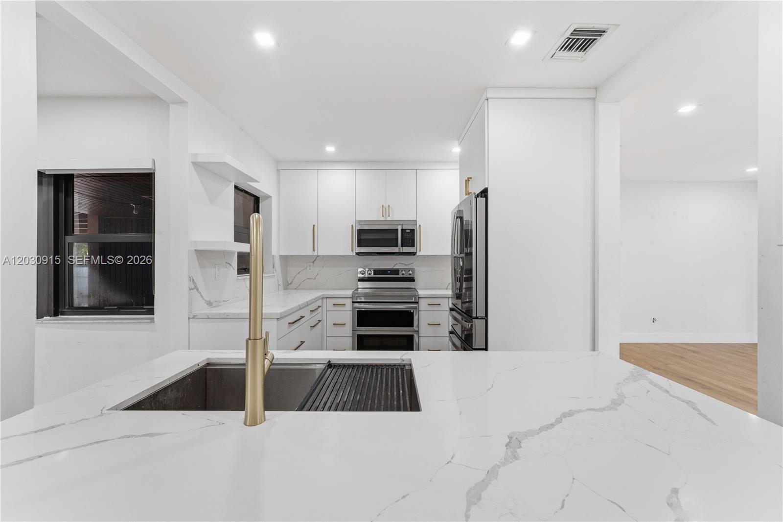 A modern kitchen features white cabinets, marble countertops, stainless steel appliances, and a gold faucet — 121 SW 71st Ave, Miami FL 33144, MIAMI, FL