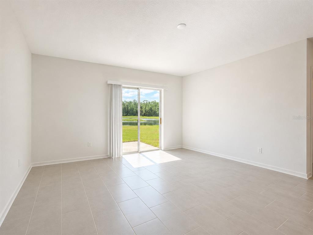 An empty room with light tile flooring and a sliding glass door overlooking a pond — 1187 CABOT CLIFFS DRIVE, DAYTONA BEACH, FL
