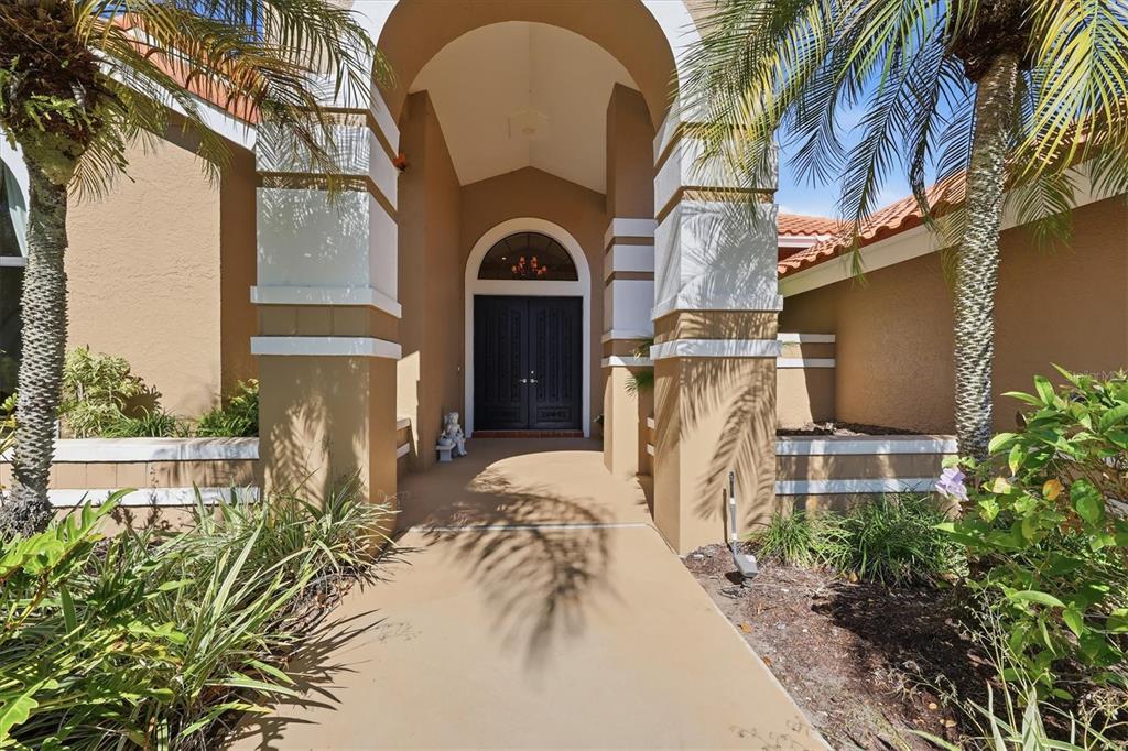 A tan house exterior features a covered entryway with double doors and palm trees — 4221 ESCONDITO CIRCLE, SARASOTA, FL