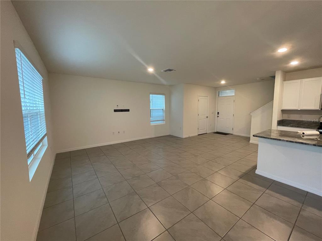 An open-concept living room features large gray floor tiles, white walls, and a kitchen counter — 33952 JASPER STONE DRIVE, WESLEY CHAPEL, FL