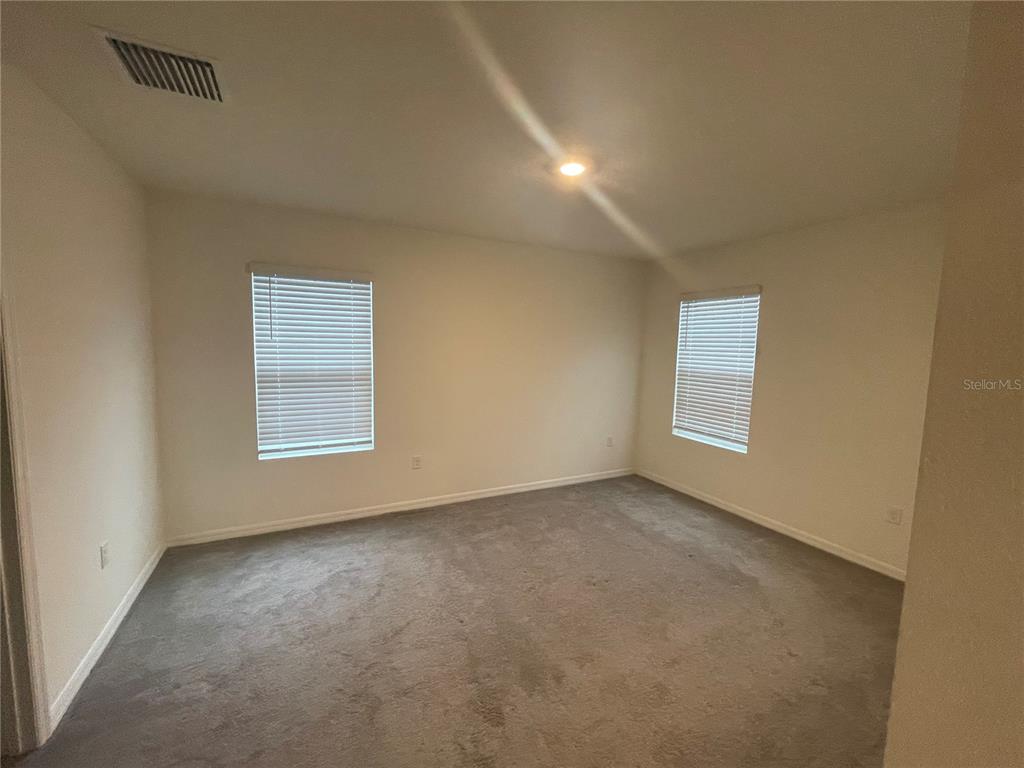 An empty bedroom features beige walls, gray carpeting, and two windows with white blinds — 33952 JASPER STONE DRIVE, WESLEY CHAPEL, FL