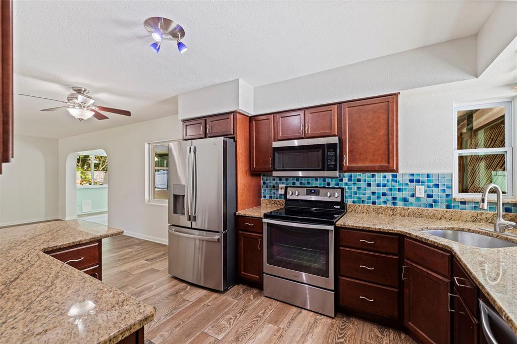 A kitchen with dark wood cabinets, granite countertops, stainless steel appliances, and blue mosaic tile — 13555 CROFT DRIVE N, LARGO, FL