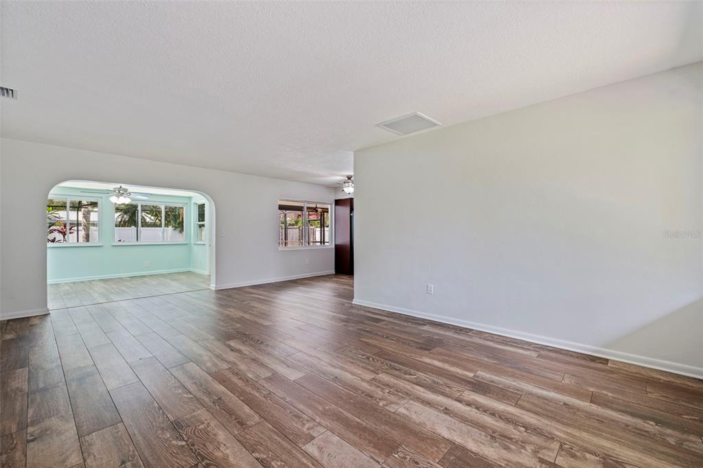 An empty living area features wood-look tile flooring and an arched opening to a sunroom — 13555 CROFT DRIVE N, LARGO, FL