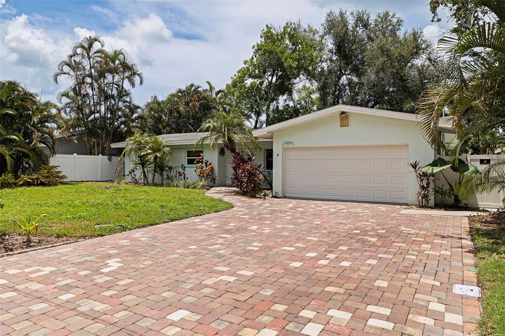 A single-story house with a light-colored exterior, a paved driveway, and lush tropical landscaping — 13555 CROFT DRIVE N, LARGO, FL