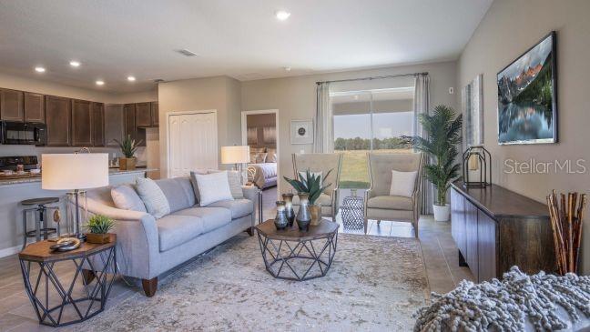 A living room with a gray sofa, two armchairs, and an open kitchen in the background — 74 ENCLAVE AVENUE, PALM COAST, FL