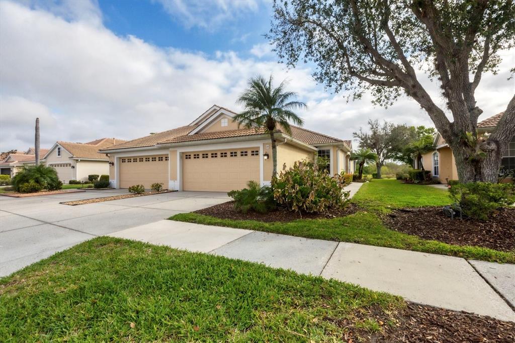 A tan, single-story house with a three-car garage and a palm tree in the front yard — 4301 WHISPERING OAKS DRIVE, NORTH PORT, FL