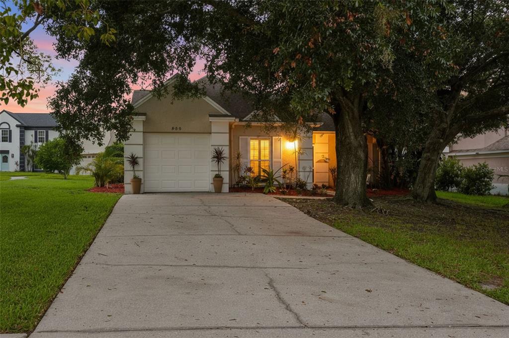 A single-story house with a white garage door, concrete driveway, and large trees in front — 934 BERKLEY COURT N, PALM HARBOR, FL