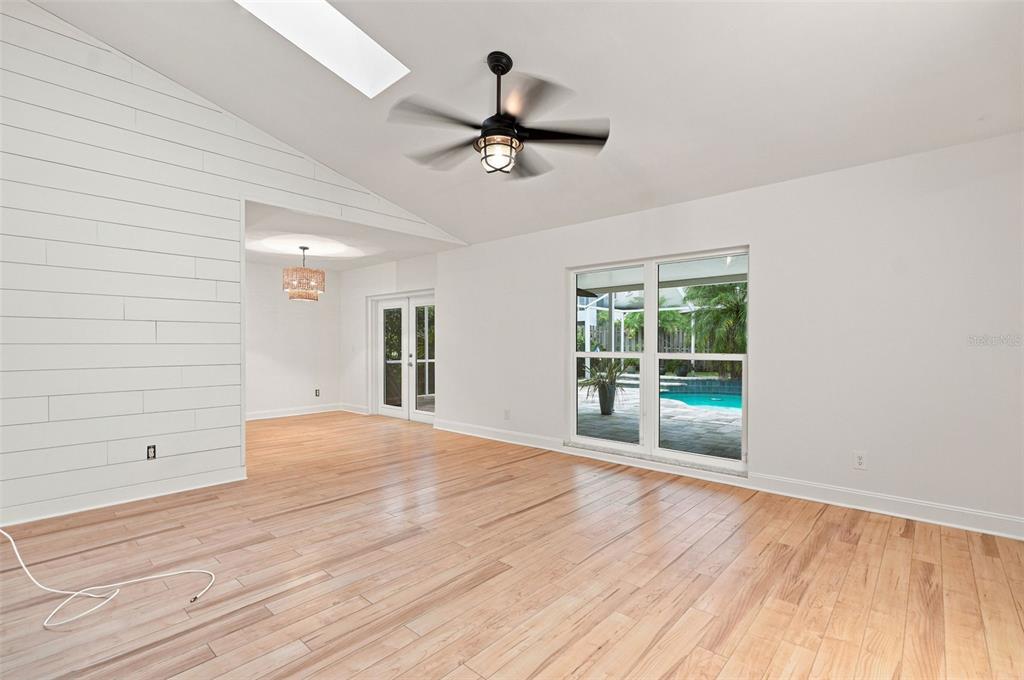 A living room with light wood floors, a shiplap wall, and a view of a pool — 934 BERKLEY COURT N, PALM HARBOR, FL