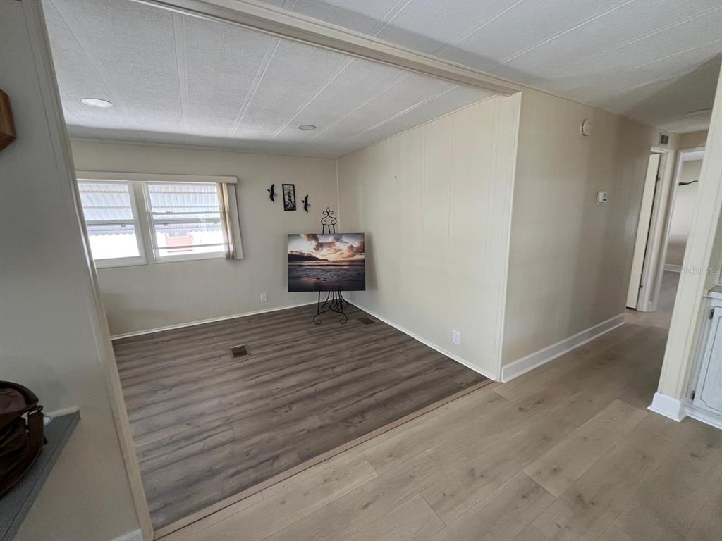A living area features light-colored walls, wood-look flooring, and a television on a metal stand — 10924 FEDERAL DRIVE, PORT RICHEY, FL