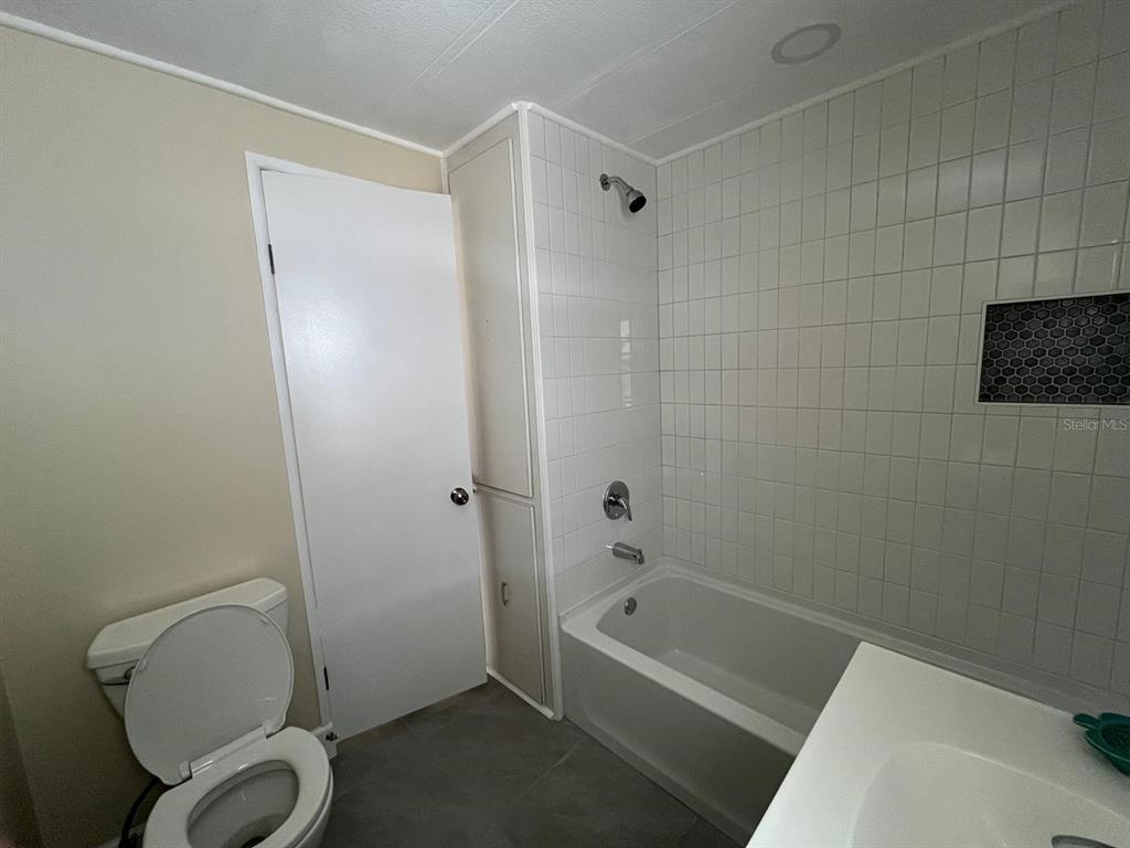 A bathroom features a white bathtub with tiled walls, a toilet, and a tall cabinet — 10924 FEDERAL DRIVE, PORT RICHEY, FL