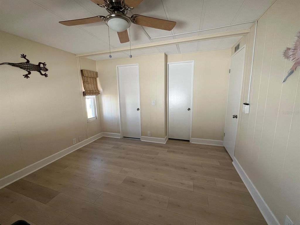 A bedroom with light-colored wood-look flooring, beige paneled walls, a ceiling fan, and three doors — 10924 FEDERAL DRIVE, PORT RICHEY, FL