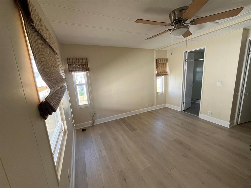 A bedroom with light wood-look flooring, beige walls, a ceiling fan, and an attached bathroom — 10924 FEDERAL DRIVE, PORT RICHEY, FL