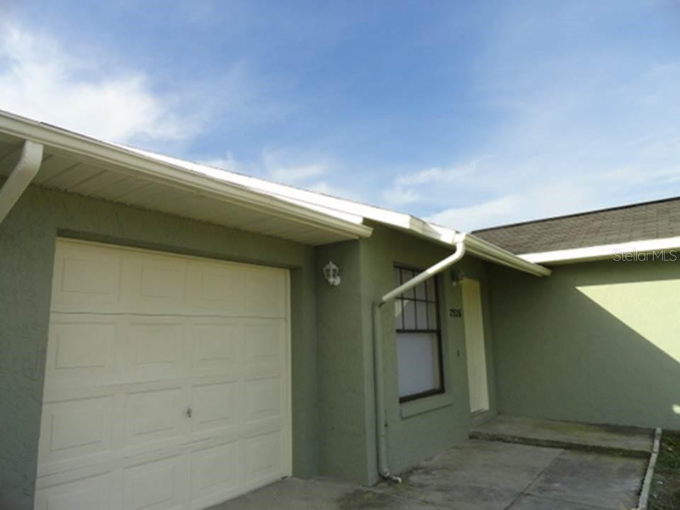A view of a house exterior featuring a garage, a front door, and a window — 7526 UNIVERSITY GARDEN DRIVE, WINTER PARK, FL