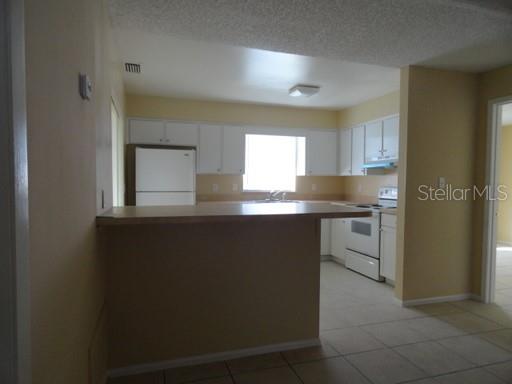 A kitchen with white cabinets, a white refrigerator, a stove, and a breakfast bar — 7526 UNIVERSITY GARDEN DRIVE, WINTER PARK, FL