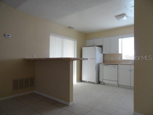 A kitchen with white cabinets, a white refrigerator, a dishwasher, and a breakfast bar — 7526 UNIVERSITY GARDEN DRIVE, WINTER PARK, FL
