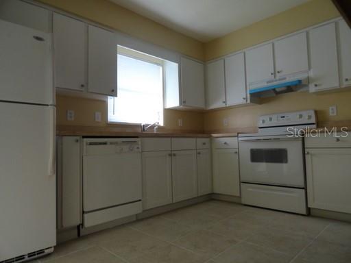 A kitchen with white cabinets, white appliances, light-colored tile flooring, and a window over the sink — 7526 UNIVERSITY GARDEN DRIVE, WINTER PARK, FL