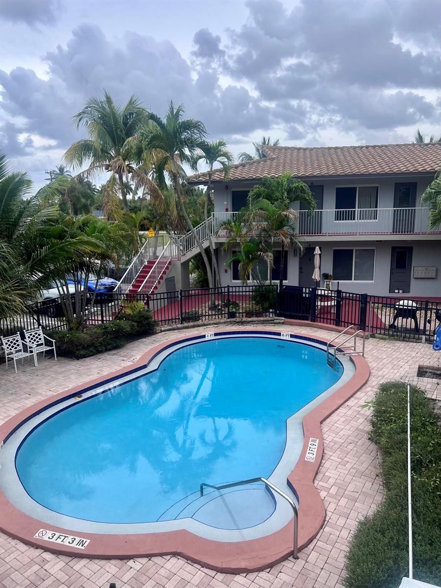 An outdoor swimming pool sits in front of a two-story apartment building with palm trees — 915 SE 22nd Avenue, Pompano Beach FL 33062, POMPANO BEACH, FL