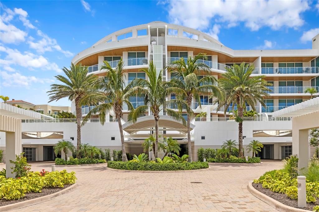 A modern multi-story residential building with a curved facade, palm trees, and a paved driveway — 2251 GULF OF MEXICO DRIVE UNIT 301, LONGBOAT KEY, FL