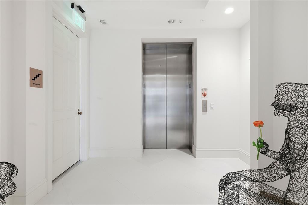 A white hallway features a stainless steel elevator, a white door, and wire art sculptures — 2251 GULF OF MEXICO DRIVE UNIT 301, LONGBOAT KEY, FL