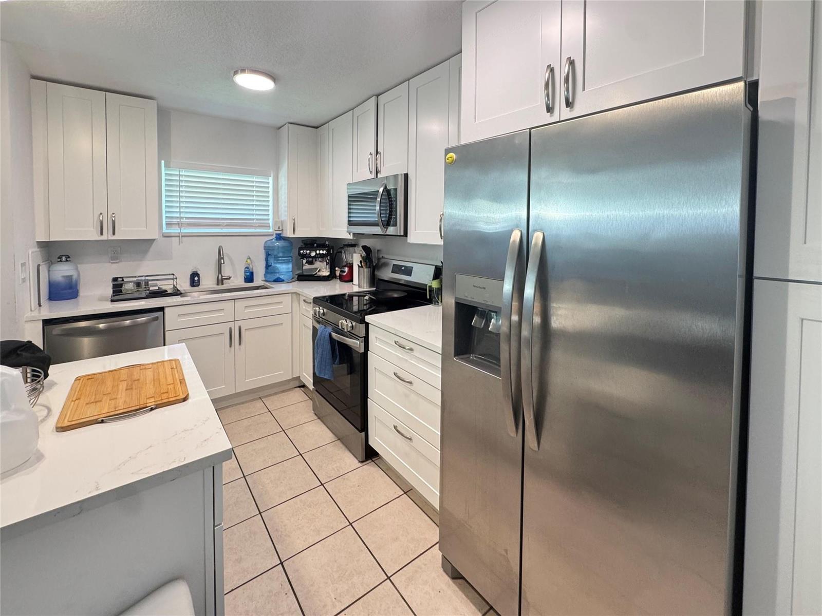 A kitchen features white cabinets, stainless steel appliances, quartz countertops, and light-colored tile flooring — 151 SW 15th Street, Pompano Beach FL 33060, POMPANO BEACH, FL