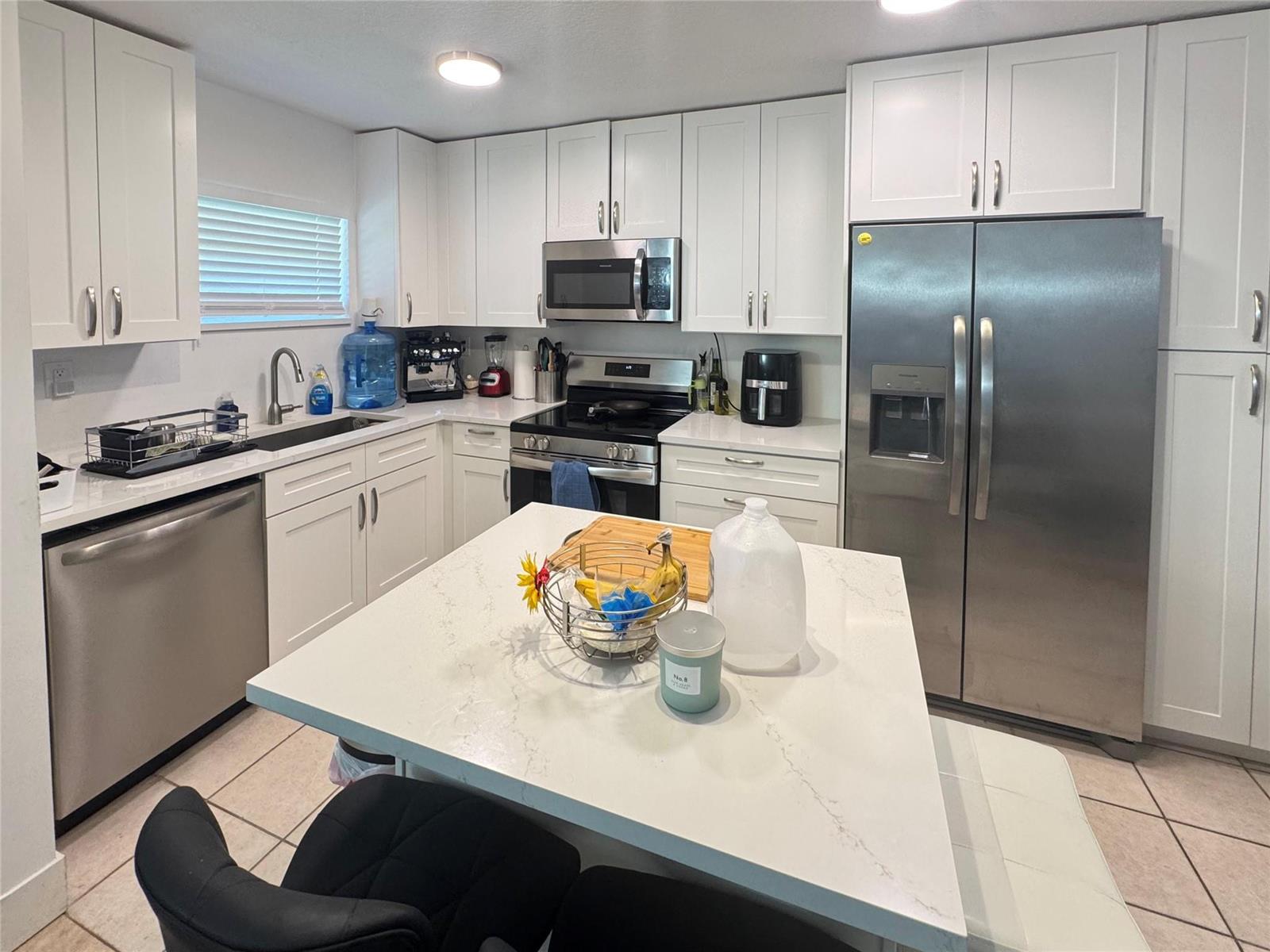 A kitchen features white cabinets, stainless steel appliances, a quartz-topped island, and tile flooring — 151 SW 15th Street, Pompano Beach FL 33060, POMPANO BEACH, FL
