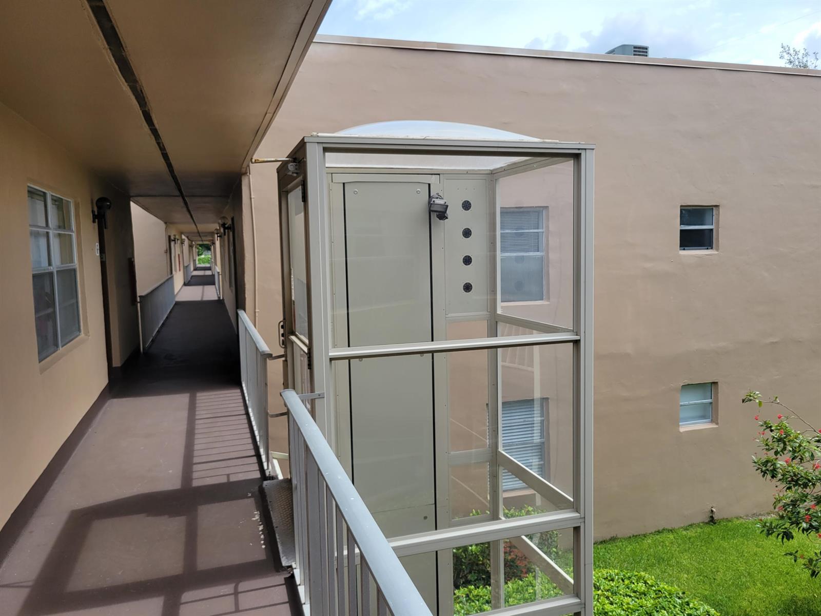 An outdoor glass elevator lift is positioned along the exterior walkway of a multi-story building — 662 Burgundy N, Delray Beach FL 33484, DELRAY BEACH, FL