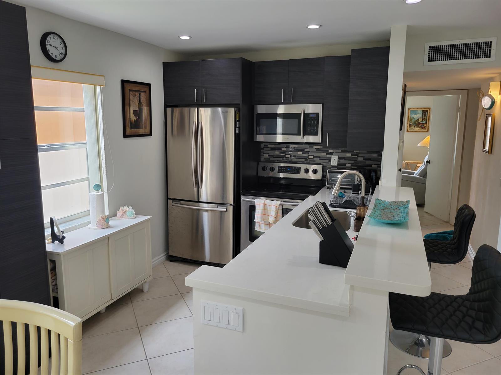 A modern kitchen features dark wood cabinets, stainless steel appliances, and a white breakfast bar — 662 Burgundy N, Delray Beach FL 33484, DELRAY BEACH, FL