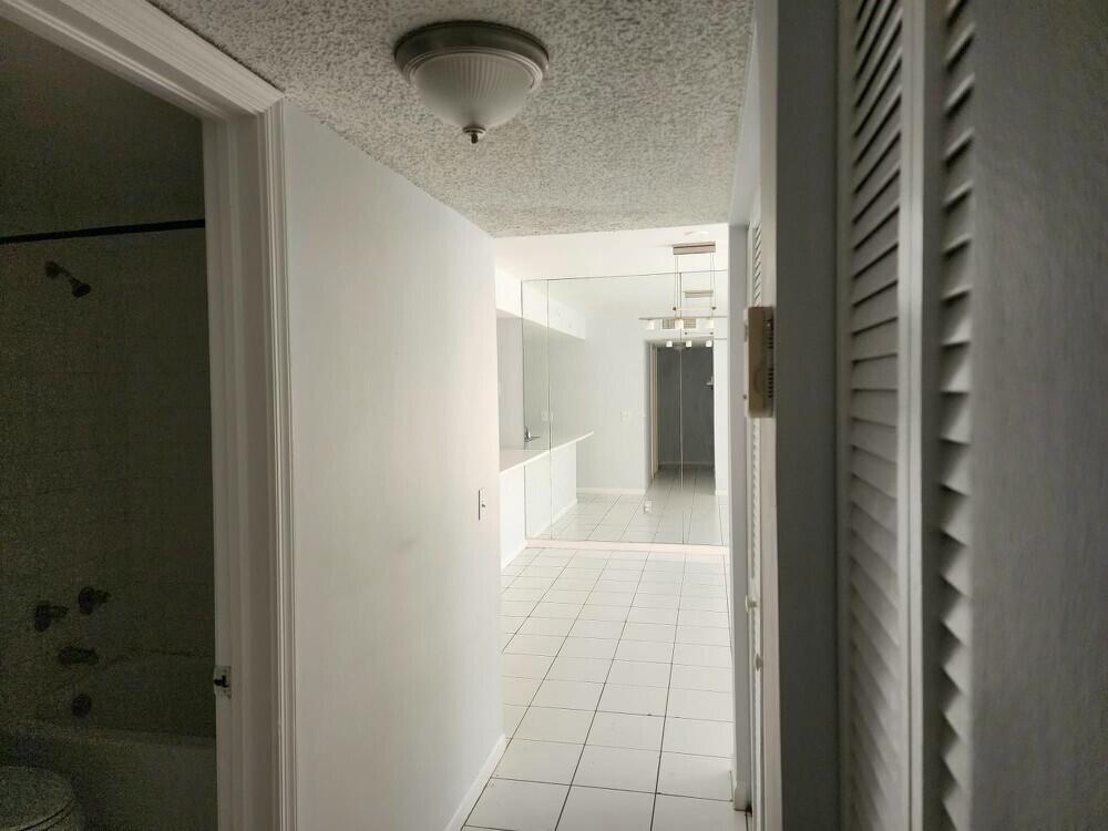 A hallway with white tile flooring leads to a kitchen area featuring mirrored walls — 176 Waterside Drive, Hypoluxo FL 33462, HYPOLUXO, FL