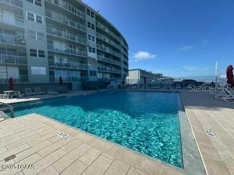 A swimming pool sits on a paved deck in front of a multi-story apartment building — 800 N ATLANTIC AVENUE UNIT 420, DAYTONA BEACH, FL