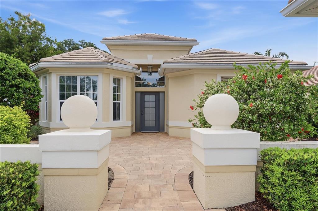 A paved walkway leads to the front entrance of a beige house with two spherical pillars — 7235 KENSINGTON COURT, UNIVERSITY PARK, FL