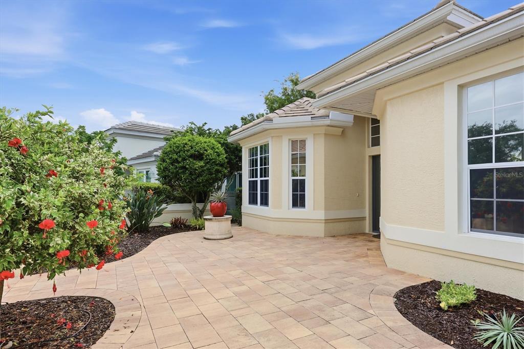 A paved patio area sits outside a beige house with a bay window and landscaping — 7235 KENSINGTON COURT, UNIVERSITY PARK, FL