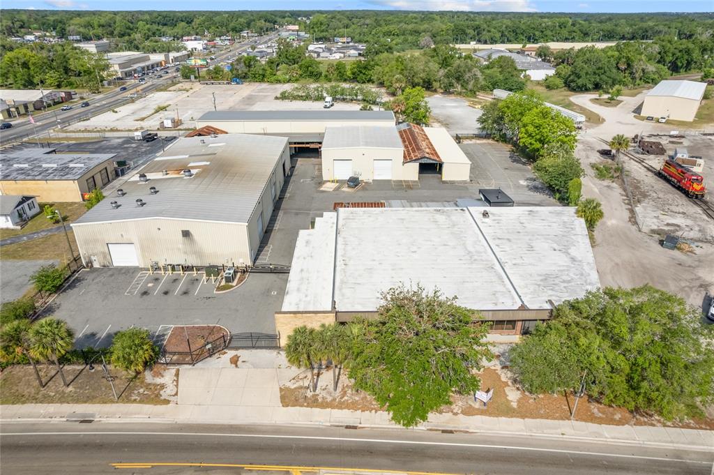 An aerial view shows industrial warehouse buildings with metal roofs and a nearby train — 1118 N MAGNOLIA AVENUE, OCALA, FL