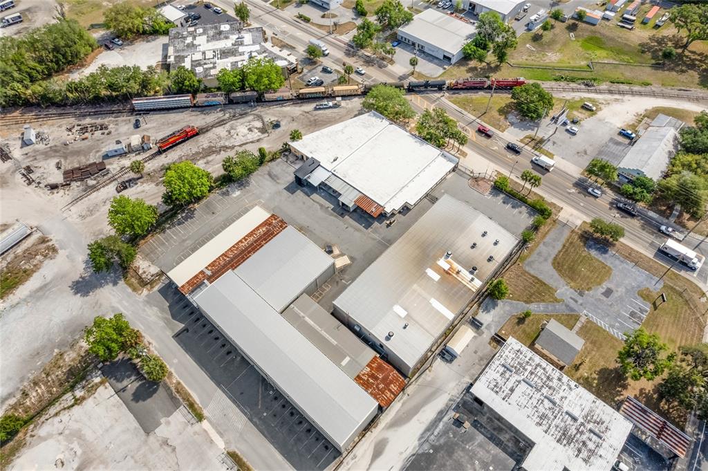 An aerial view shows industrial warehouse buildings, a railroad track with trains, and surrounding roads — 1118 N MAGNOLIA AVENUE, OCALA, FL