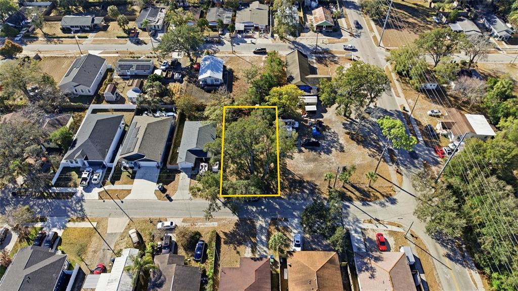 An aerial view shows a vacant, tree-covered lot outlined in yellow within a residential neighborhood — 3405 E POWHATAN AVENUE, TAMPA, FL