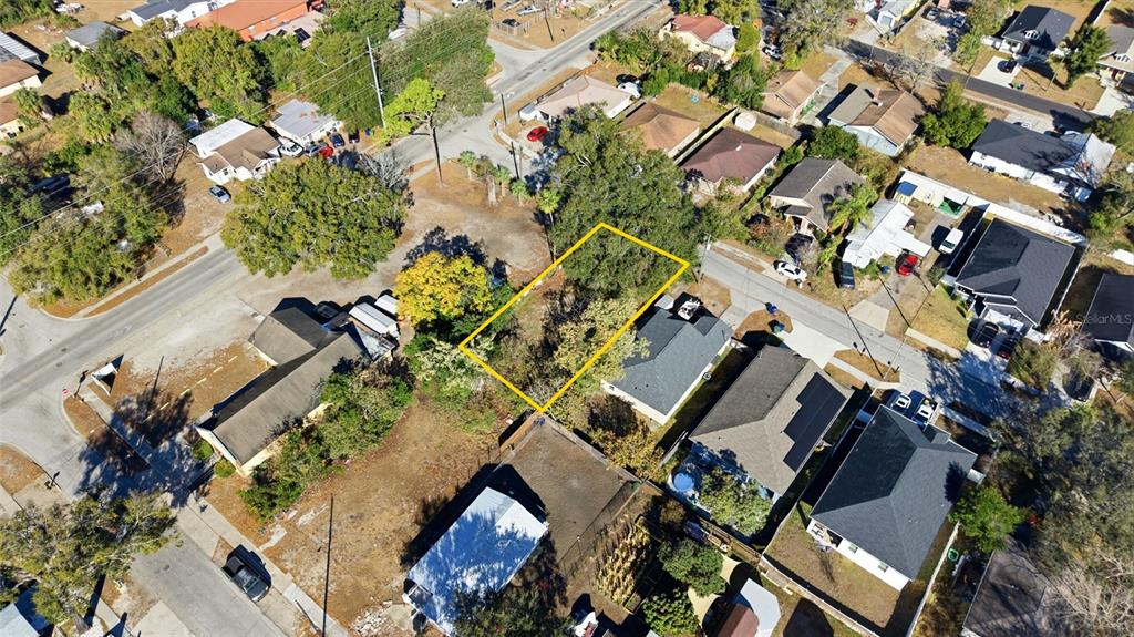 An aerial view shows a vacant, tree-covered residential lot outlined in yellow — 3405 E POWHATAN AVENUE, TAMPA, FL