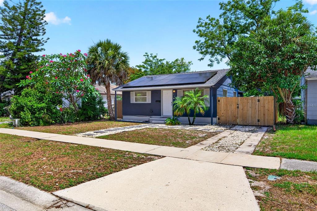 A single-story house with dark blue siding, a solar panel roof, and a wooden fence — 4616 9TH AVENUE S, ST PETERSBURG, FL