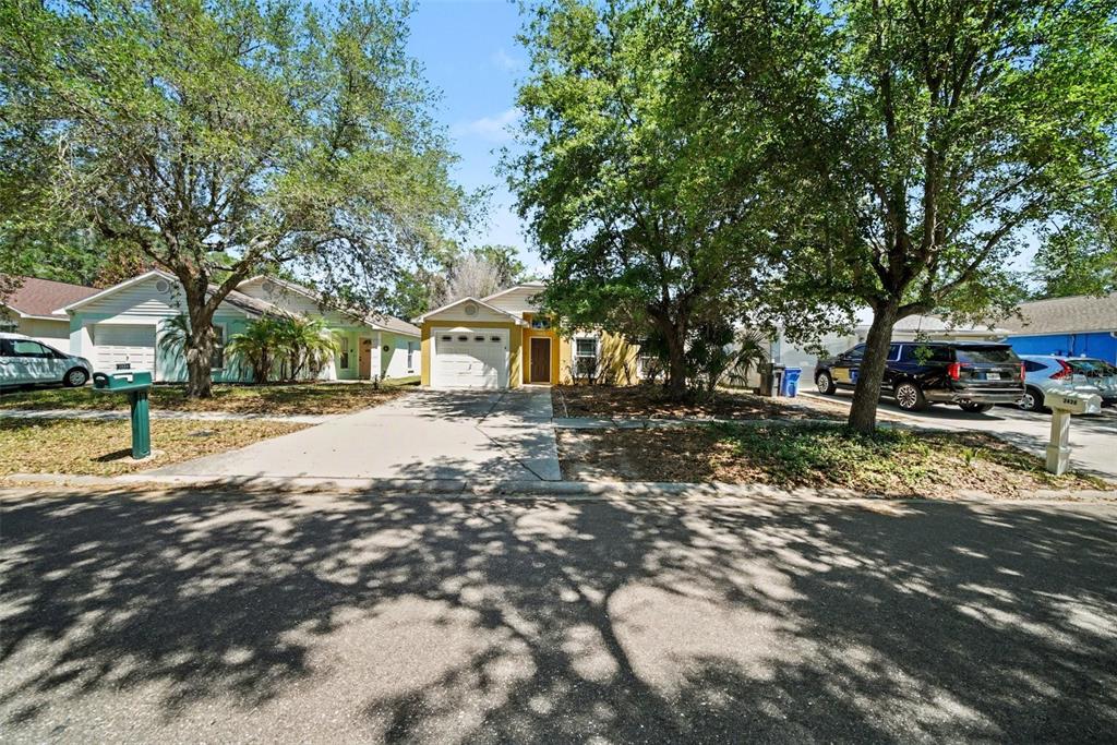 A single-story house with a garage and driveway sits behind large trees on a street — 2424 CAMDEN OAKS PLACE, VALRICO, FL