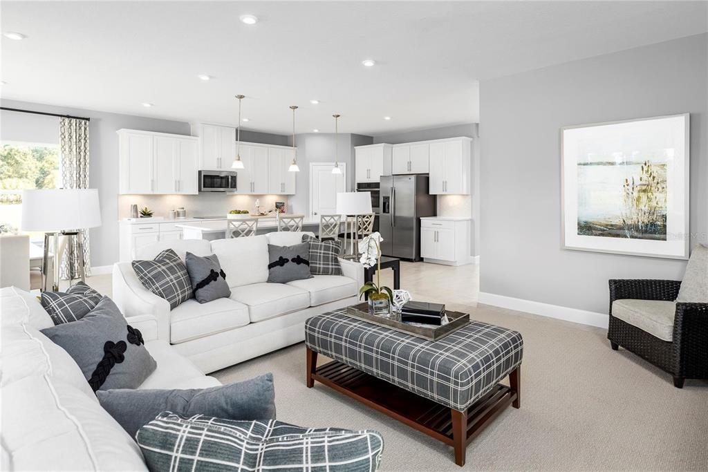 A living room with white sofas and a plaid ottoman opens to a white kitchen — 443 HAMMOCK OAKS BOULEVARD, LADY LAKE, FL