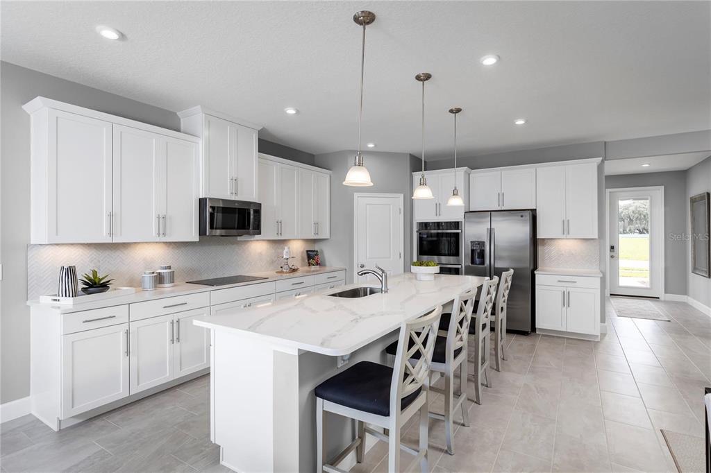 A modern kitchen features white cabinetry, a marble-topped island with seating, and stainless steel appliances — 443 HAMMOCK OAKS BOULEVARD, LADY LAKE, FL