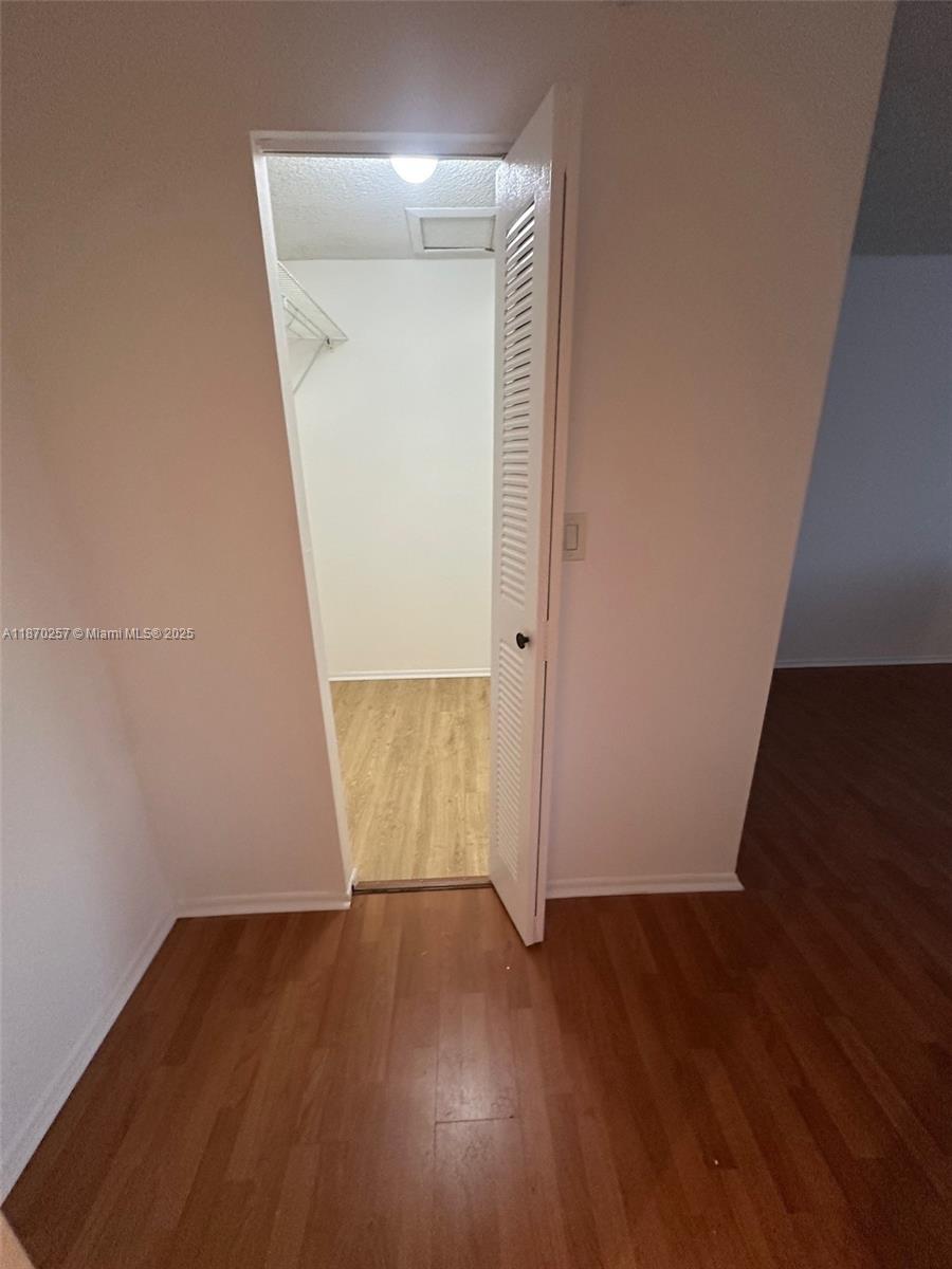 A closet with wood-look flooring and a white louvered door opens into a room — 17911 NW 68th Ave # N206, Hialeah FL 33015, HIALEAH, FL