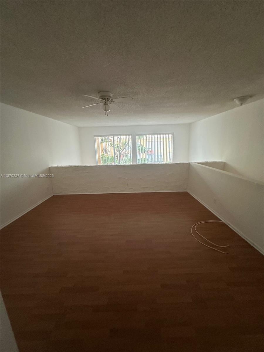 An empty room features wood-look flooring, white walls, a ceiling fan, and large windows — 17911 NW 68th Ave # N206, Hialeah FL 33015, HIALEAH, FL