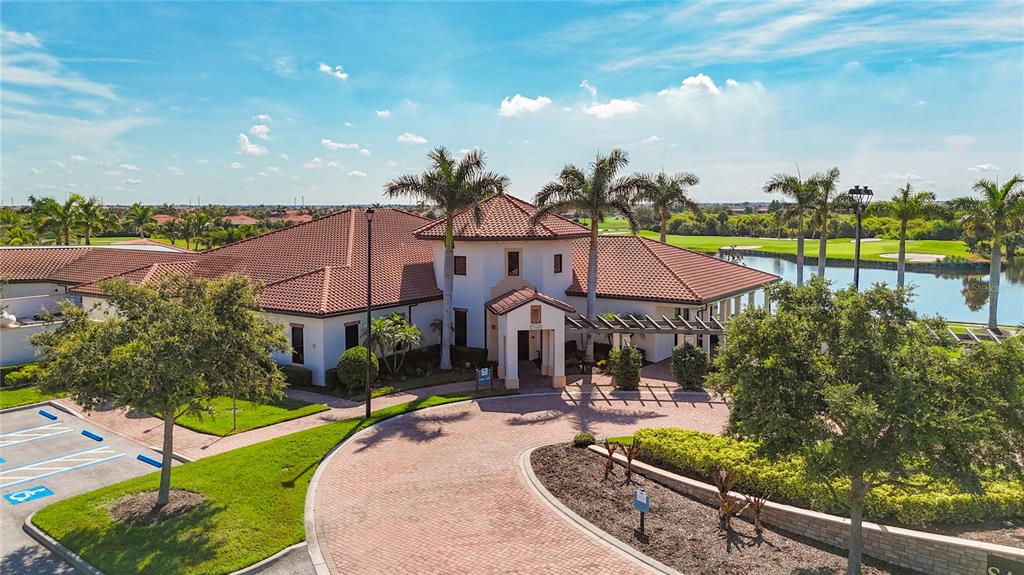 An aerial view of a clubhouse with a red tile roof, circular driveway, and pond — 24137 SPARTINA DRIVE, VENICE, FL