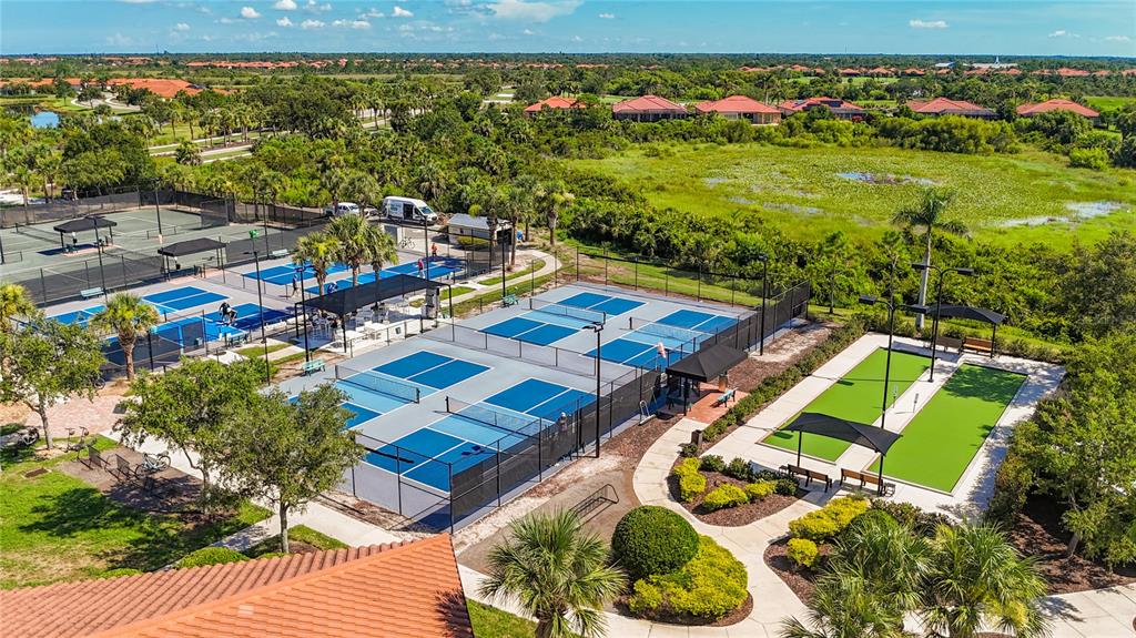 An aerial view shows outdoor pickleball courts and bocce ball courts surrounded by lush landscaping — 24137 SPARTINA DRIVE, VENICE, FL