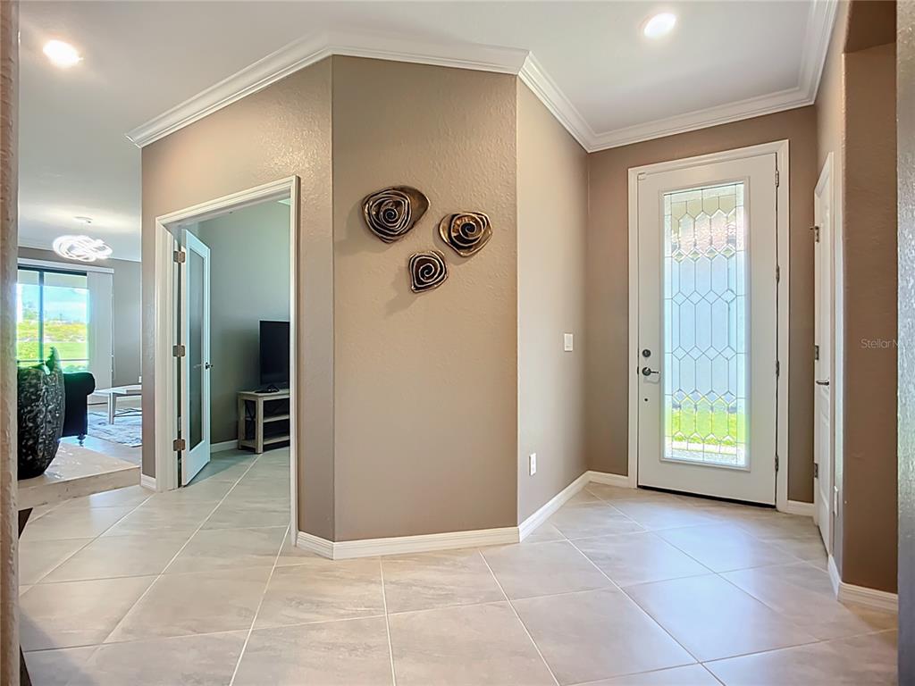 An entryway with tile flooring, a glass-paneled front door, and a wall with decorative accents — 24137 SPARTINA DRIVE, VENICE, FL