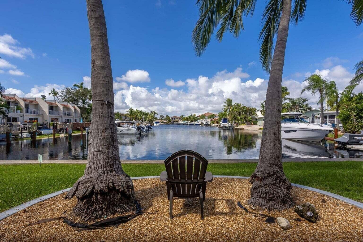 A brown chair sits on a gravel patch between two palm trees overlooking a canal — 1880 SE 3rd Street # 1880, Pompano Beach FL 33060, POMPANO BEACH, FL