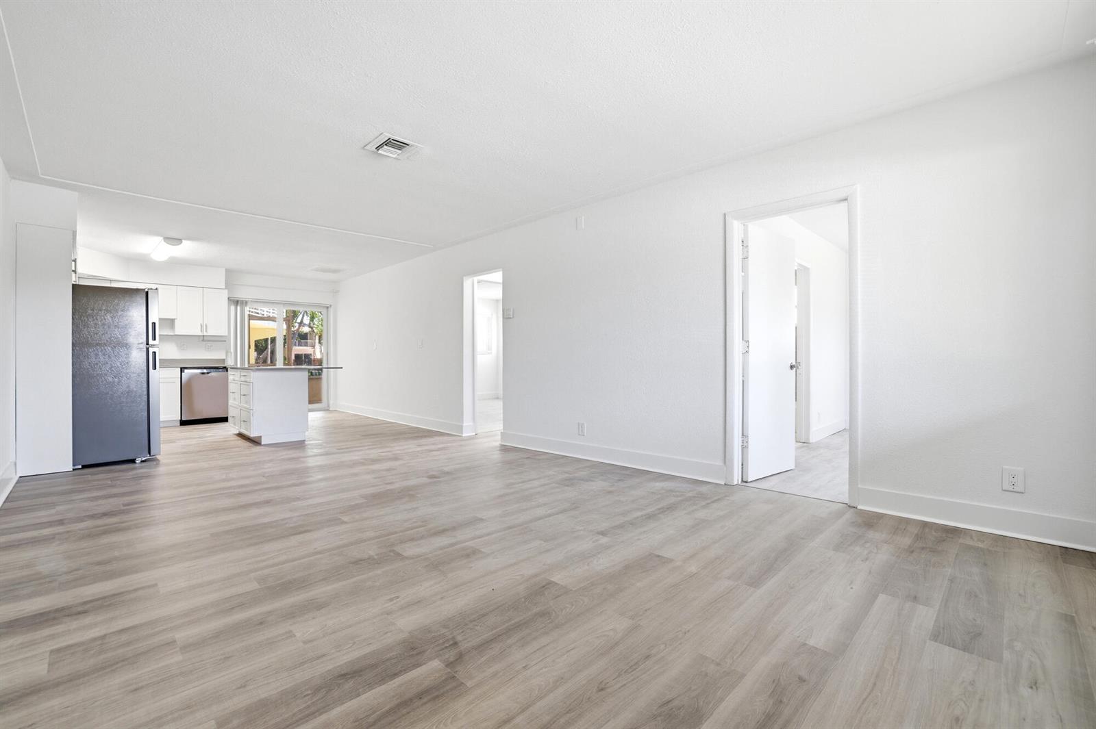 An open-concept living area with light wood-look flooring leads to a kitchen with stainless appliances — 1880 SE 3rd Street # 1880, Pompano Beach FL 33060, POMPANO BEACH, FL